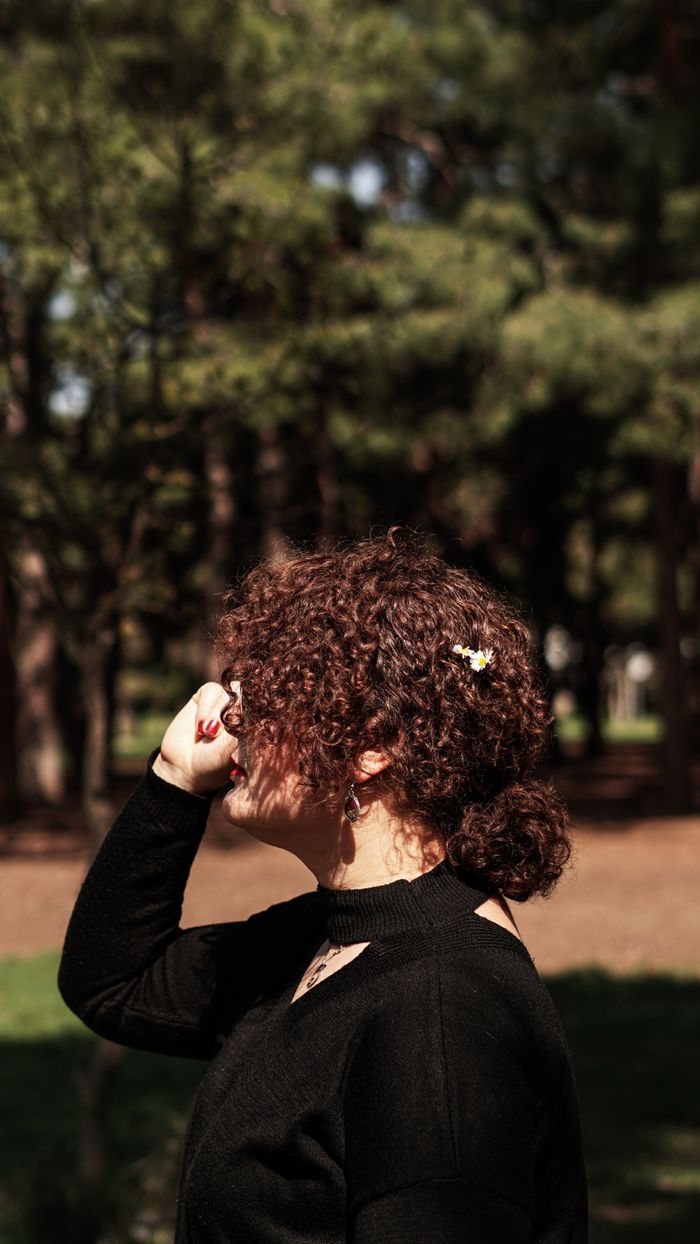 A woman enjoys the sunny day in a summer park, surrounded by lush green trees.