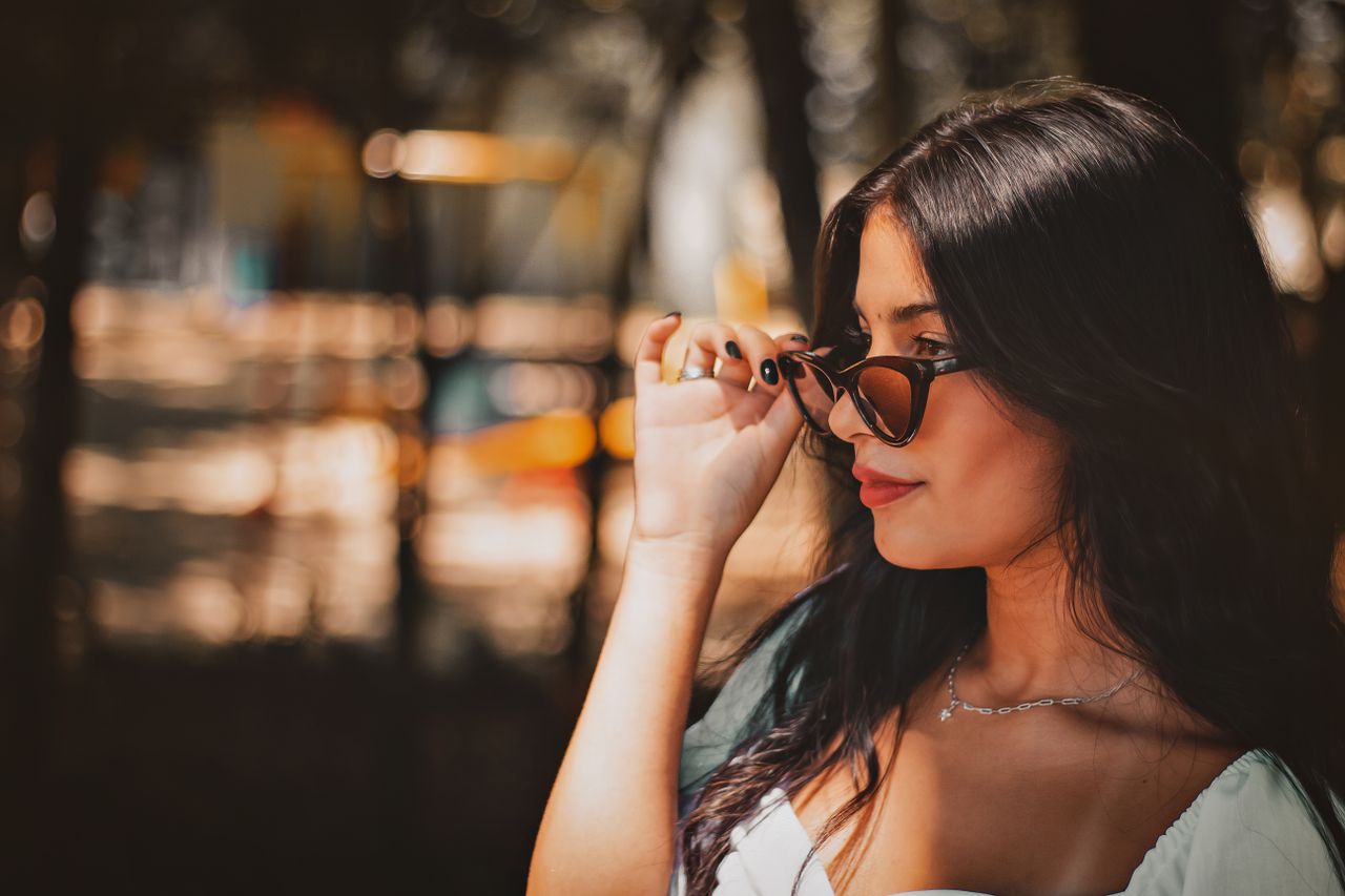 A young brunette woman in sunglasses enjoys the warm sunlight outdoors. Perfect for lifestyle and fashion concepts.