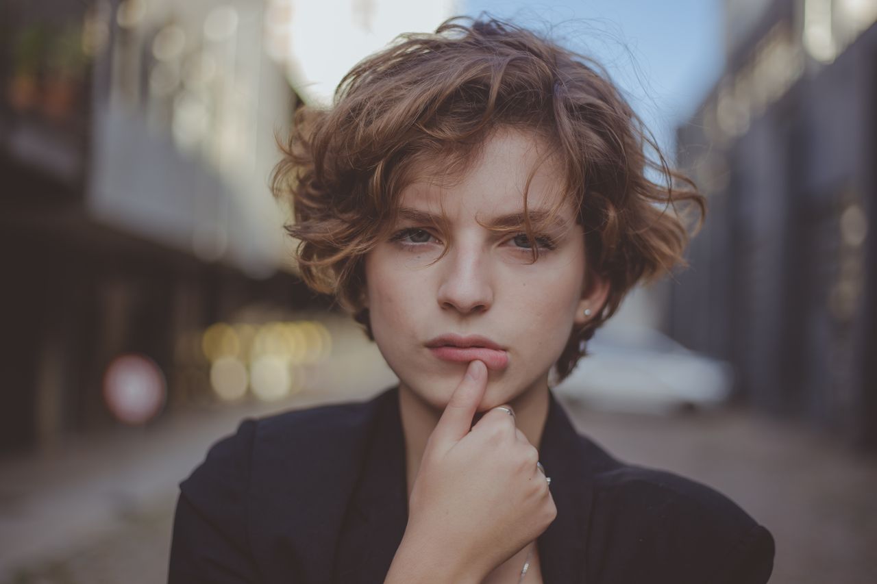 Close-up portrait of a woman with short hair, looking thoughtful in an urban setting.