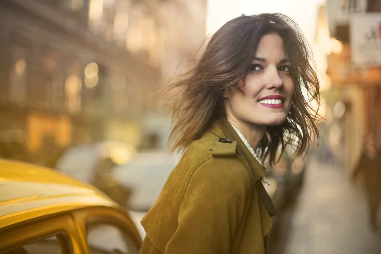 Smiling woman in a coat enjoying a walk on a sunny city street.