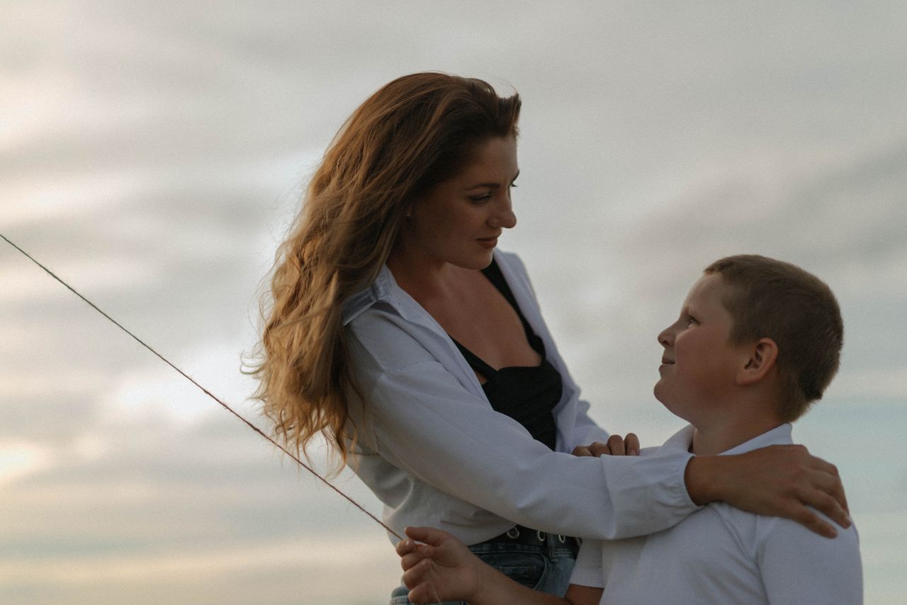 An affectionate moment between a mother and her son under a cloudy sky.